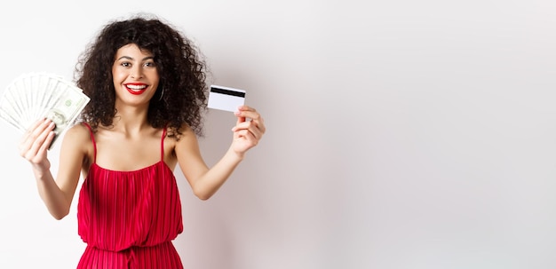 Foto grátis comprando mulher sortuda em vestido elegante mostrando dinheiro e cartão de crédito de plástico sorrindo satisfeito usando