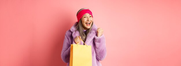 Compras e conceito de moda feliz mulher asiática sênior ganhando segurando saco de papel e fazendo bomba de punho