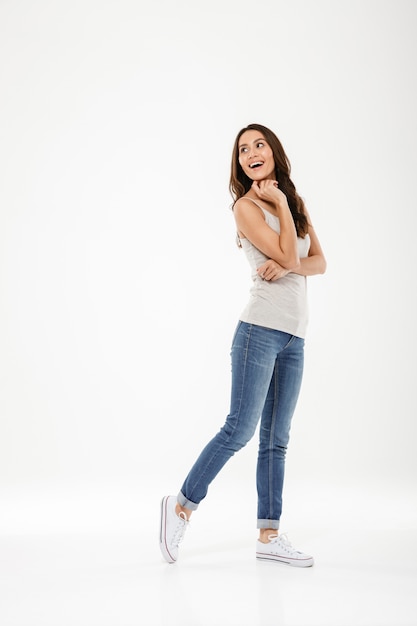 Foto grátis comprimento total de mulher morena feliz posando e olhando para trás sobre cinza