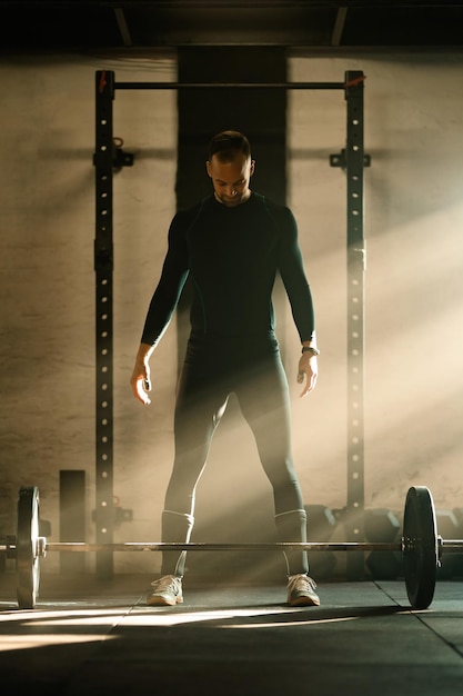 Foto grátis comprimento total do homem de construção muscular concentrando-se antes de levantar uma barra durante o treinamento de força em uma academia