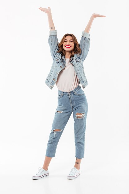 Comprimento total mulher feliz em roupas jeans se divertindo sobre parede branca