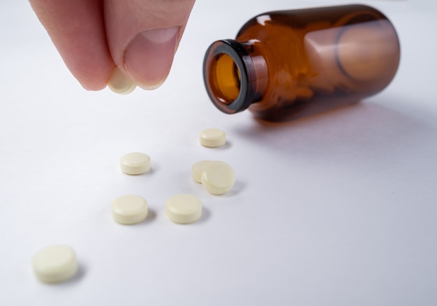 Comprimidos brancos estão espalhados ao lado do frasco sobre a mesa, close-up de um comprimido na mão