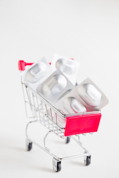 Comprimidos da bolha da tira no carrinho de compras diminuto no fundo branco