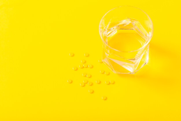Comprimidos de medicamento pequeno e copo de água sobre o fundo amarelo