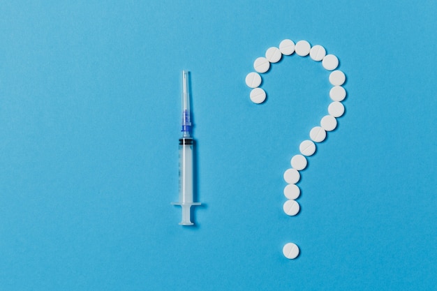 Comprimidos redondos brancos de medicação dispostos em forma de ponto de interrogação isolado em um fundo de cor azul