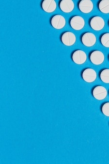 Comprimidos redondos brancos de medicação dispostos em um triângulo isolado em um fundo de cor azul