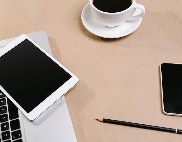 Computador portátil, bloco de notas, tablet e uma xícara de café expresso em cima da mesa