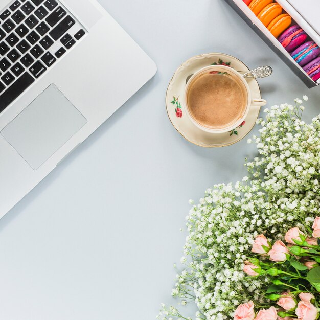 Computador portátil; xícara de café; Macaroons e buquê de flores sobre fundo branco