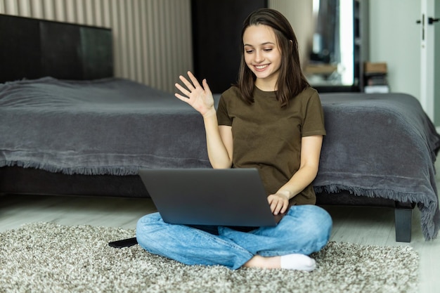 Comunicação à distância. Mulher jovem com fones de ouvido fazendo videochamada no laptop em casa