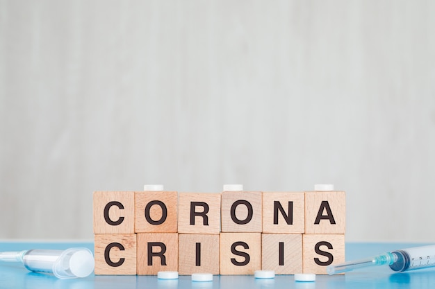 Conceito da crise do Coronavirus com cubos de madeira, comprimidos médicos, seringa na opinião lateral da tabela azul e cinzenta.