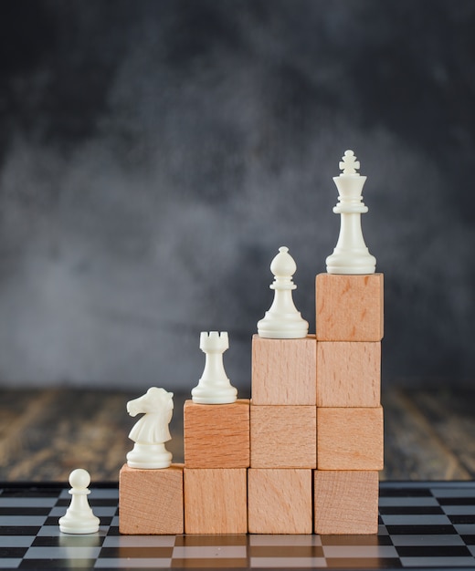 Conceito da hierarquia do negócio com tabuleiro de xadrez, figuras na pirâmide de blocos de madeira na opinião lateral da tabela nevoenta e de madeira.