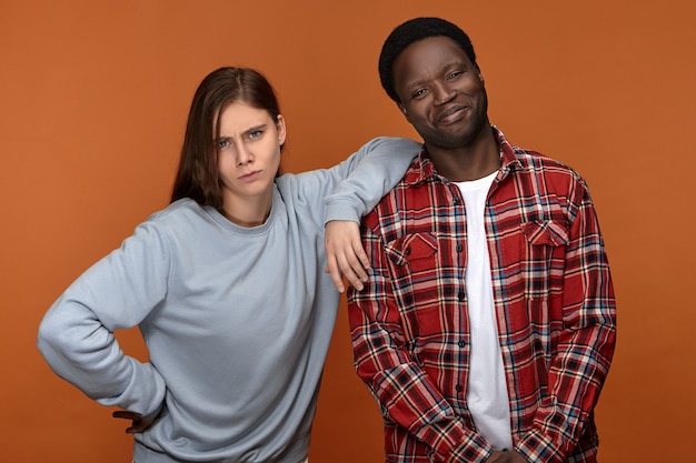 Foto grátis conceito de alegria e felicidade. casal interracial emocional apaixonado, se divertindo. um negro jovem bonito e feliz rindo enquanto sua namorada branca engraçada coloca o cotovelo em seu ombro