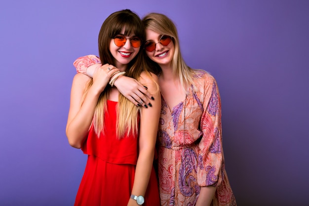 Conceito de amizade e comunicação, duas irmãs melhores meninas de frondes vestindo colocar combinando com abraços da cômoda de verão da moda e looks na câmera, óculos boho, fundo roxo.