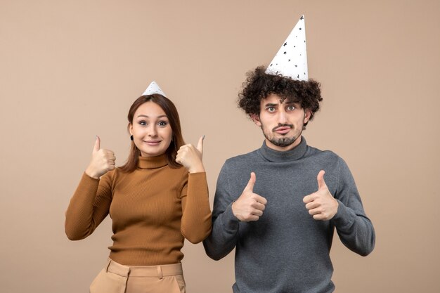 Conceito de ano novo com jovem casal satisfeito usando garota de chapéu de ano novo e cara fazendo gesto de ok em cinza