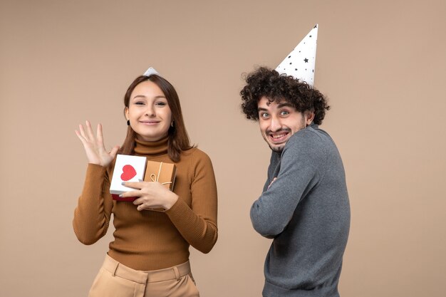 Conceito de ano novo com jovem casal usando chapéu de ano novo garota feliz com coração e presente e cara sorridente em cinza