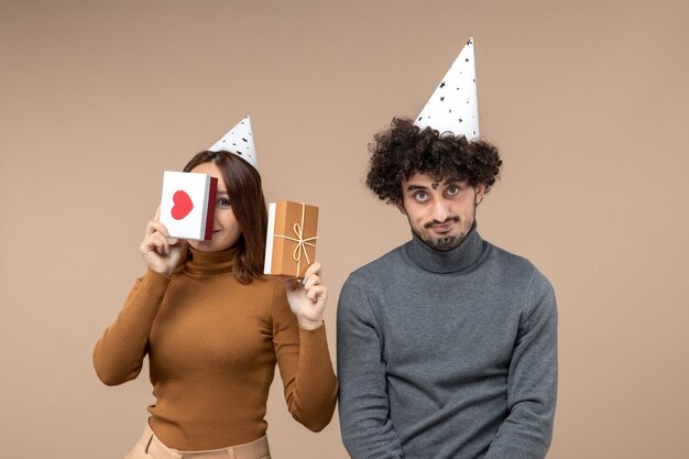 Conceito de ano novo com jovem casal usando garota de chapéu de ano novo fechando o rosto coração e presente e cara insatisfeito