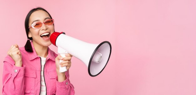 Conceito de anúncio de atenção Menina asiática entusiasmada gritando em publicidade de megafone com orador recrutando em pé sobre fundo rosa