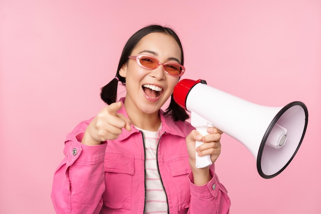Conceito de anúncio de atenção menina asiática entusiasmada gritando em publicidade de megafone com orador recrutando em pé sobre fundo rosa