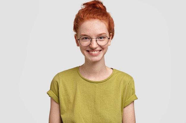 Conceito de beleza e emoções naturais. Garota feliz e despreocupada com sardas e sorriso terno, feliz por passar no exame, usa camiseta casual e óculos, modelos contra a parede branca, tem cabelo sexy