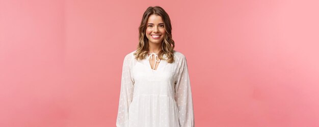 Conceito de beleza e mulheres de primavera Retrato de uma menina loira feminina tenra com um sorriso radiante branco em um vestido leve e bonito sobre fundo rosa com emoções positivas de atitude feliz