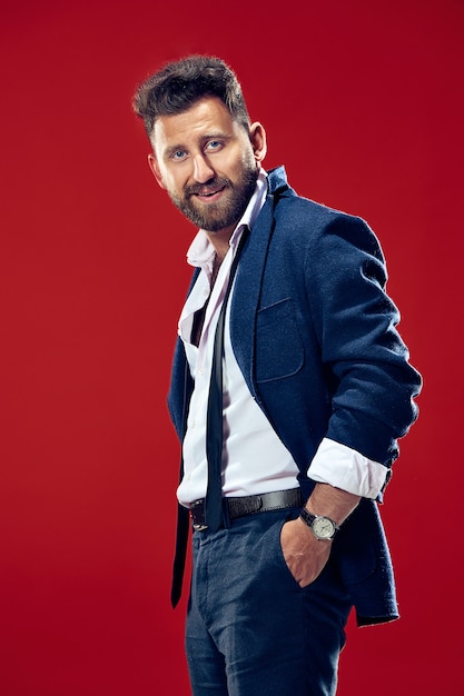 Foto grátis conceito de beleza masculina. retrato de um jovem elegante com corte de cabelo elegante, vestindo terno da moda posando sobre fundo vermelho. cabelo perfeito. estilo italiano elegante.