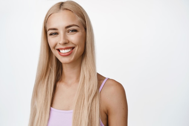 Foto grátis conceito de bem-estar e pessoas close-up de loira atraente sorrindo com dentes brancos, olhando para a câmera feliz em pé na regata sobre fundo branco