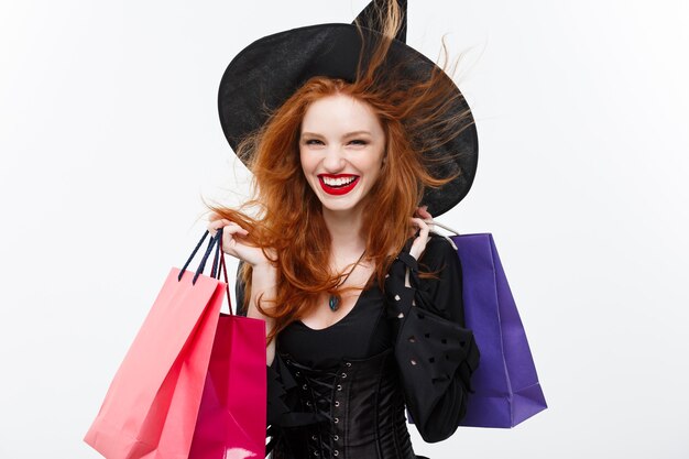 Conceito de bruxa de Halloween bruxa feliz de Halloween sorrindo e segurando sacolas de compras coloridas na parede branca