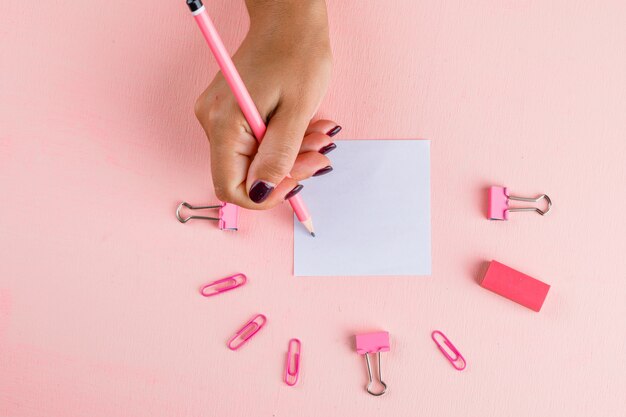 Conceito de celebração com clipes de papel e fichário, borracha na mesa-de-rosa plana plana leigos. mulher escrevendo na nota auto-adesiva.