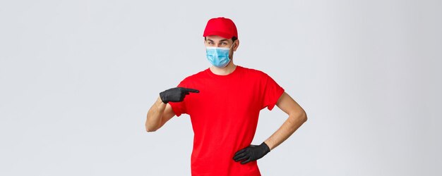Conceito de compras on-line de autoquarentena Covid19 Entregador sorridente confiante em luvas de máscara facial de uniforme apontando a si mesmo Courier fornece transporte rápido durante surto de coronavírus