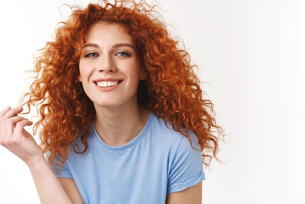 Conceito de cuidados capilares de beleza de ternura sedutora jovem sensual com cabelo ruivo encaracolado natural rolando o fio no dedo bobo sorrindo dentuço olhando feliz e coquete fundo branco em pé