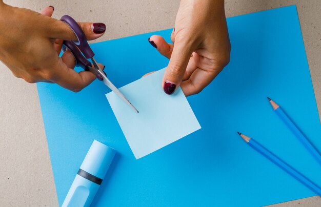 Conceito de educação com material escolar em papel, plana leigos. mulher cortando nota auto-adesiva.