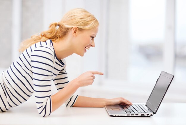 Conceito de educação e internet - aluna sorridente apontando o dedo para a tela do laptop na faculdade