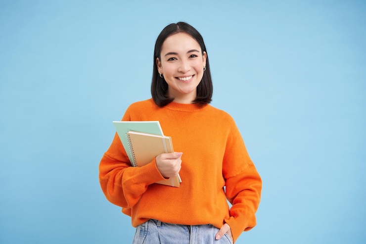 Foto grátis conceito de educação jovem asiática sorridente com notebooks parecendo felizes com o estudante de câmera indo para