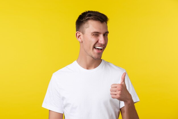 Conceito de emoções de estilo de vida, verão e pessoas. homem feliz bonito atrevido em t-shirt branca, piscando e polegar para cima, elogiando o bom trabalho, muito bem, parabéns pela conquista.