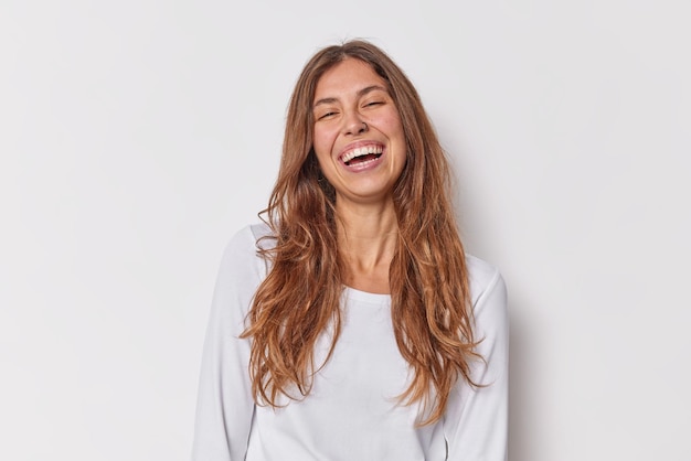 Foto grátis conceito de emoções humanas positivas jovem europeia de cabelos compridos com sorrisos penetrantes, vestida com um jumper casual isolado sobre fundo branco modelo feminino alegre posa em estúdio