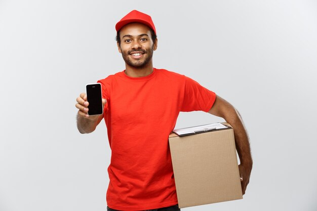 Conceito de entrega - Retrato de Handsome African American Delivery Man ou courier com caixa mostrando tablet em você para verificar a ordem. Isolado no fundo do estúdio cinzento. Espaço de cópia.