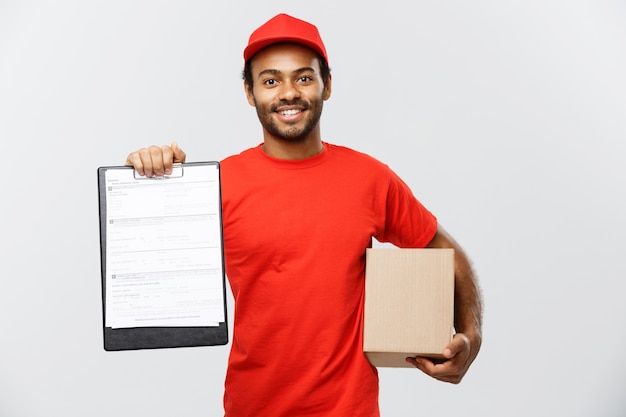 Conceito de entrega - Retrato do homem de entrega afro-americano bonito ou de um mensageiro que mostra um formulário de documento de confirmação para assinar. Isolado no fundo do estúdio cinzento. Espaço de cópia.