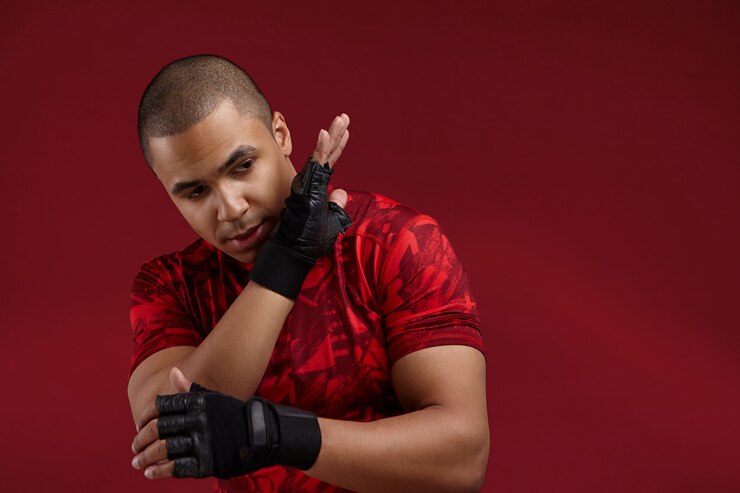 Foto grátis conceito de esportes e artes marciais. foto horizontal de um jovem boxeador africano forte vestindo uma camiseta vermelha e luvas sem dedos de treinamento de boxe tailandês, dominando suas habilidades na academia, com foco na expressão facial