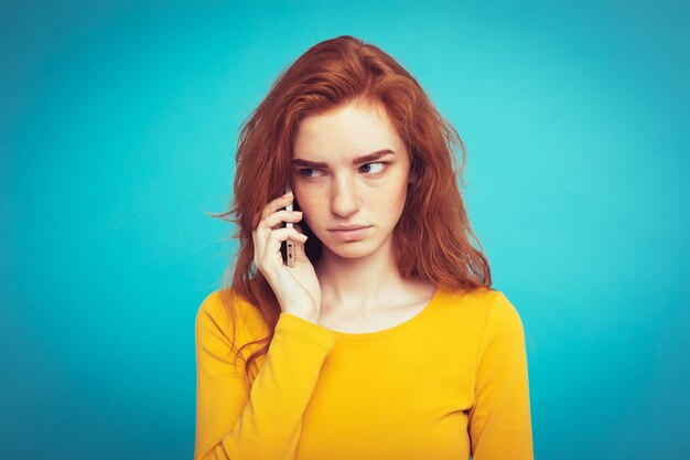 Conceito de estilo de vida - Retrato de menina de cabelo vermelho gengibre com expressão chocante e estressante enquanto conversa com um amigo por telefone celular. Isolado no fundo do Pastel azul. Copie o espaço.