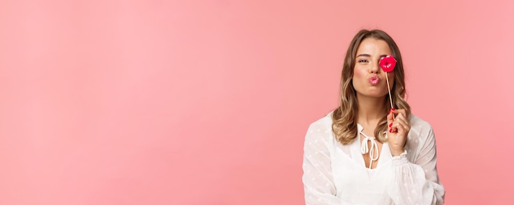 Foto grátis conceito de felicidade e celebração da primavera closeup retrato de uma linda garota loira feminina no vestido branco, dobrando os lábios no beijo e segurando o bastão de papelão festejando se divertindo no fundo rosa