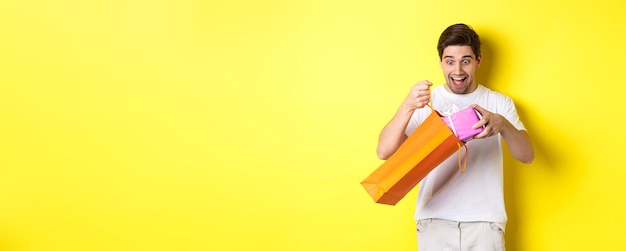 Foto grátis conceito de feriados e celebração jovem parecendo surpreso ao tirar presente da sacola de compras s