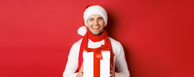 Conceito de férias de inverno natal e estilo de vida bonito homem atrevido com chapéu de papai noel e cachecol segurando