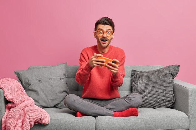 Conceito de internet e jogos de tecnologia. Homem caucasiano empolgado joga jogo no smartphone e olha para a câmera de forma surpreendente
