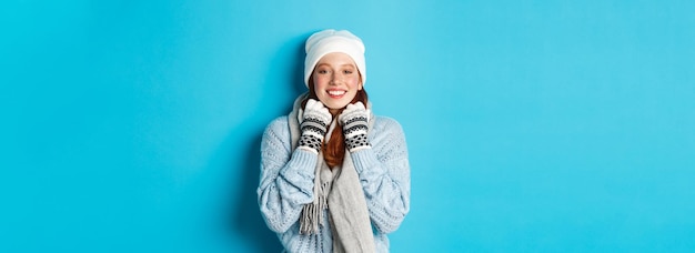 Foto grátis conceito de inverno e férias ruiva bonitinha com gorro branco e luvas sorrindo para a câmera olhando d