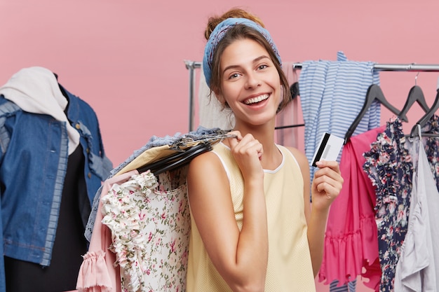 Foto grátis conceito de juventude, moda, estilo e felicidade. encantadora jovem mulher branca segurando o cartão de certificado, desfrutando de compras em boutiques de roupas, escolhendo roupas de verão, sentindo-se feliz e animada