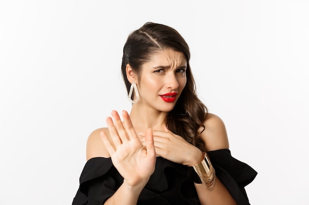 Foto grátis conceito de moda e beleza. close de uma jovem descontente em um vestido preto dizendo não, recusando a oferta e olhando com desdém, de pé sobre um fundo branco