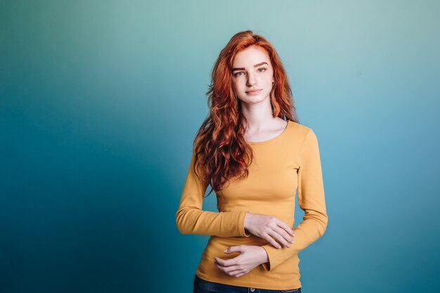 Conceito de moda - Headshot Retrato de feliz gengibre menina de cabelo vermelho com suéter amarelo com rosto confiante olhando a câmera. Pastel filme fundo azul. Espaço de cópia.