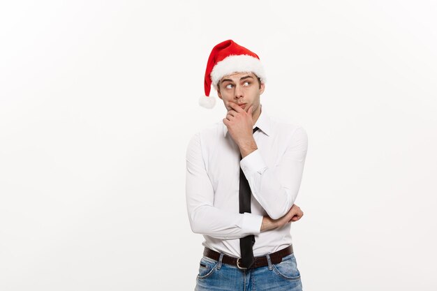 Conceito de Natal Homem de negócios bonito usa chapéu de Papai Noel posando com expressão facial pensativa em fundo branco isolado