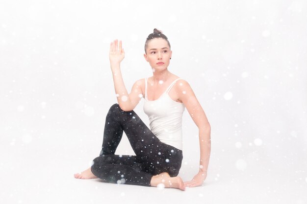 Conceito de neve, inverno, natal, fitness, esporte, treinamento e estilo de vida - jovem mulher fazendo exercícios de ioga. retrato de uma jovem linda em um sportswear branco fazendo ioga sobre um fundo de neve.