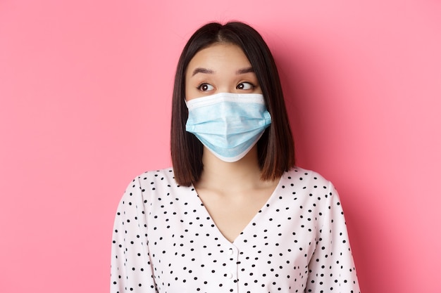 Conceito de pandemia e estilo de vida Covid belo modelo feminino asiático na máscara médica, olhando para a esquerda na co ...